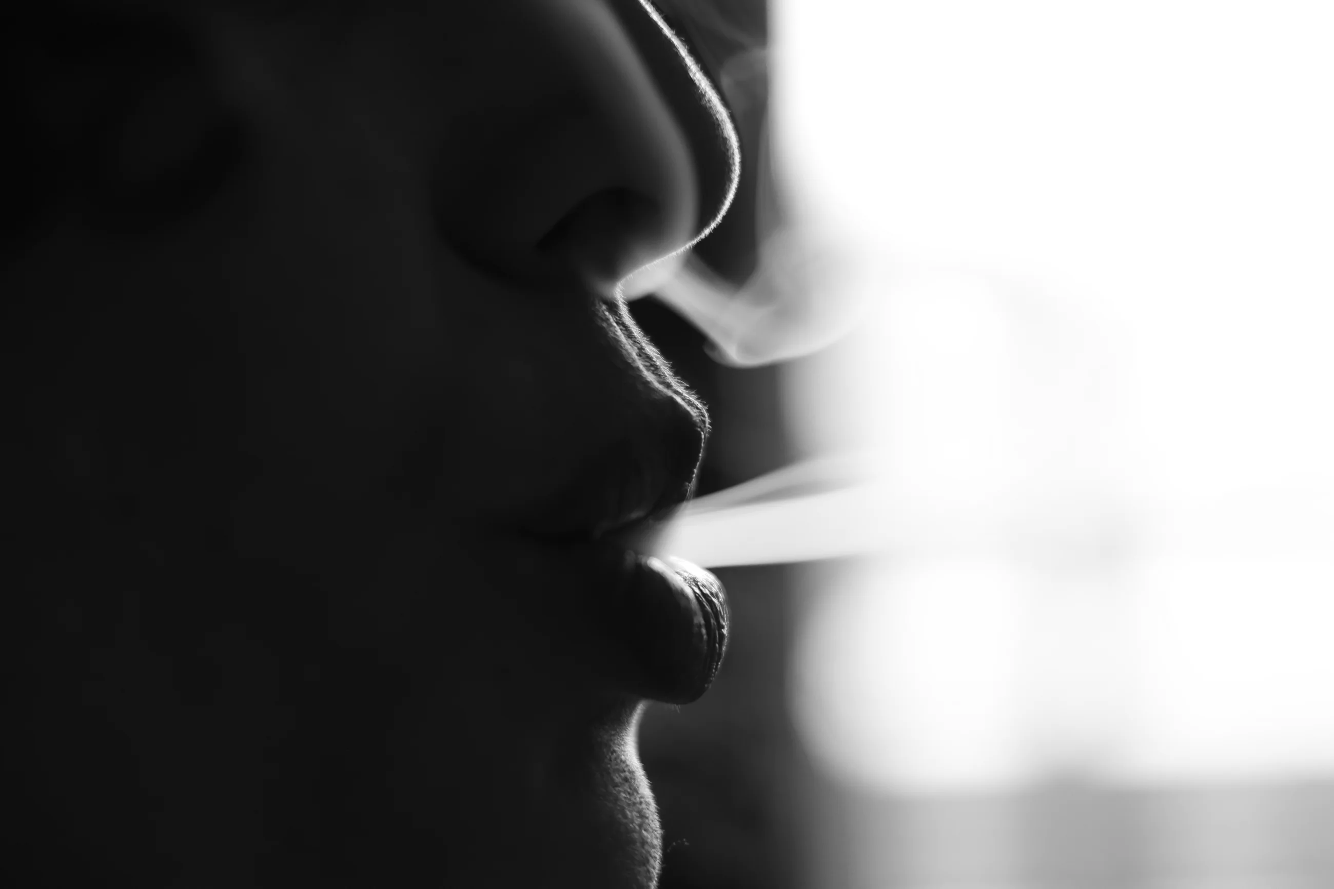 Gros plan en noir et blanc des lèvres d’une femme avec de la fumée